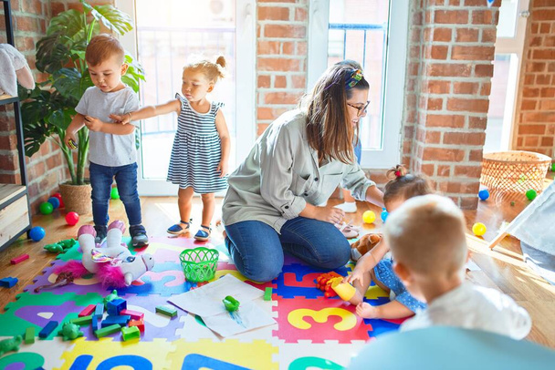 Beautiful teacher and group of toddlers playing around lots of toys at kindergarten - Photo, Image
