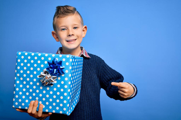 Young little caucasian kid holding surprise box as birthday or Christmas present very happy pointing with hand and finger - Fotoğraf, Görsel