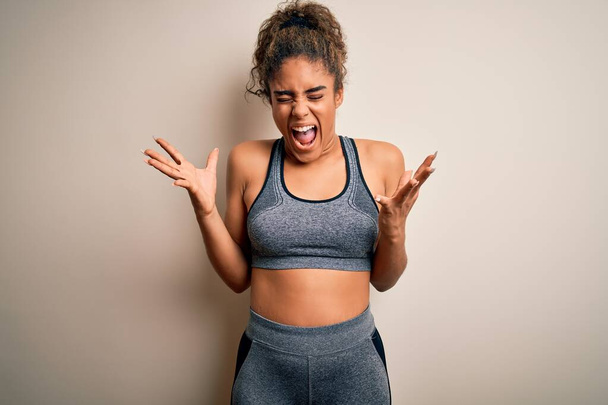 Young african american sportswoman doing sport wearing sportswear over white background celebrating mad and crazy for success with arms raised and closed eyes screaming excited. Winner concept - Foto, Imagem
