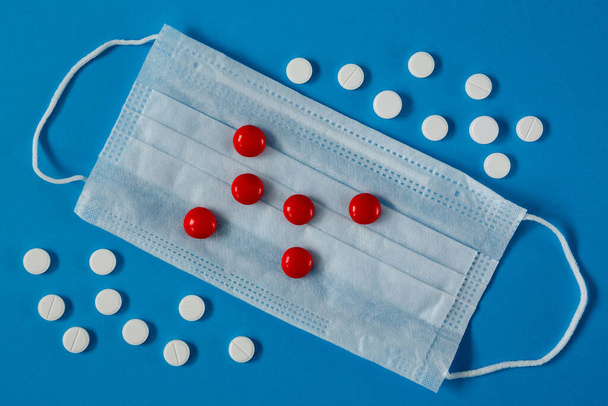lékařská maska na obličeji a bílé a červené pilulky, na modrém pozadí shora - Fotografie, Obrázek