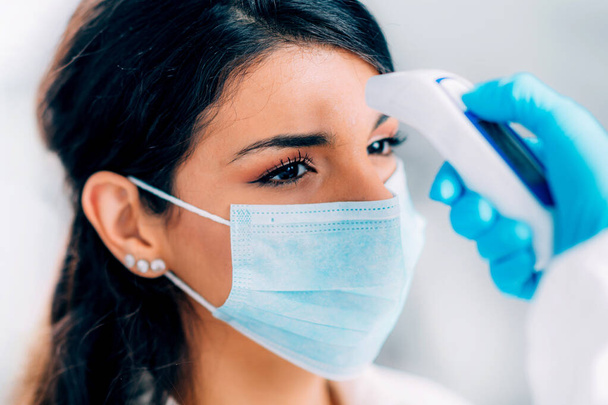 Koronavírus. Orvosi dolgozó vegyvédelmi lakosztály ellenőrzése testhőmérséklet, nő védő maszkkal - Fotó, kép