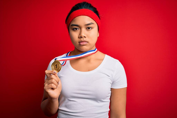 Genç Asyalı şampiyon kız madalyayı kazandı. İzole edilmiş kırmızı arka planda duruyordu. Akıllı yüzünde kendine güvenen bir ifade vardı. - Fotoğraf, Görsel