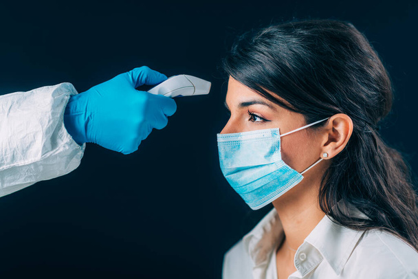Coronavirus. Medizinisches Personal in Schutzanzügen zur Überprüfung der Körpertemperatur, Frau mit Schutzmaske - Foto, Bild