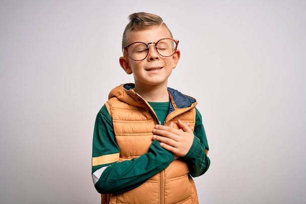Young little caucasian kid with blue eyes wearing winter coat and smart glasses smiling with hands on chest with closed eyes and grateful gesture on face. Health concept. - Foto, Imagem