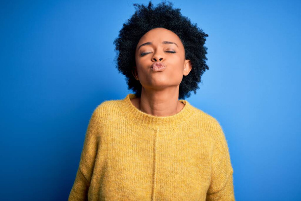Young beautiful African American afro woman with curly hair wearing yellow casual sweater looking at the camera blowing a kiss on air being lovely and sexy. Love expression. - Foto, Imagem