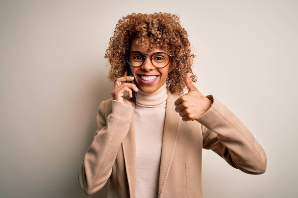 Mladá africká Američanka s kudrnatou konverzaci mluví na smartphone šťastný s velkým úsměvem dělá ok znamení, palec nahoru s prsty, vynikající znamení - Fotografie, Obrázek