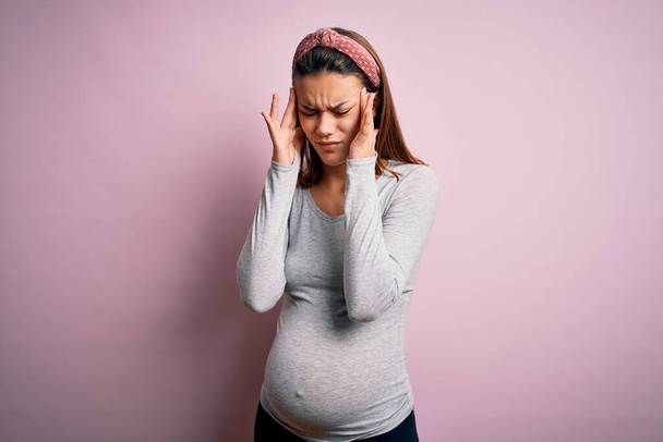 Joven hermosa adolescente embarazada esperando bebé sobre fondo rosa aislado con la mano en el dolor de cabeza porque el estrés. Dolor de migraña
. - Foto, Imagen