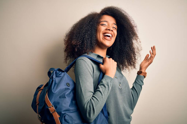 Молодая африканская студентка-американка с афроволосами в рюкзаке на заднем плане очень счастлива и взволнована, выражение победителя празднует победу крича с большой улыбкой и поднятыми руками
 - Фото, изображение