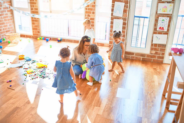 Воспитатель и группа малышей играют вокруг множества игрушек одновременно.
 - Фото, изображение