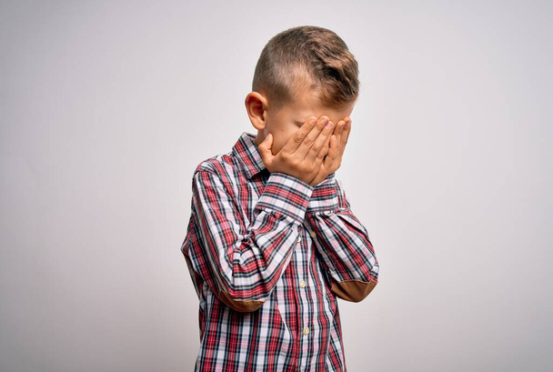 青い目の若い白人の子供は、泣きながら手で顔を覆う悲しい表情で孤立した背景の上にエレガントなシャツを着ています。うつ病の概念. - 写真・画像