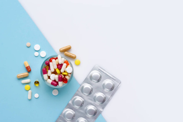 A glass full of pills, tablets, capsules on blue and white background, with empty space for text. Top view - Photo, Image
