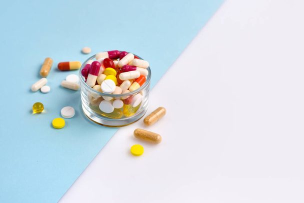 Ein Glas voller Pillen, Tabletten, Kapseln auf blauem und weißem Hintergrund - Foto, Bild