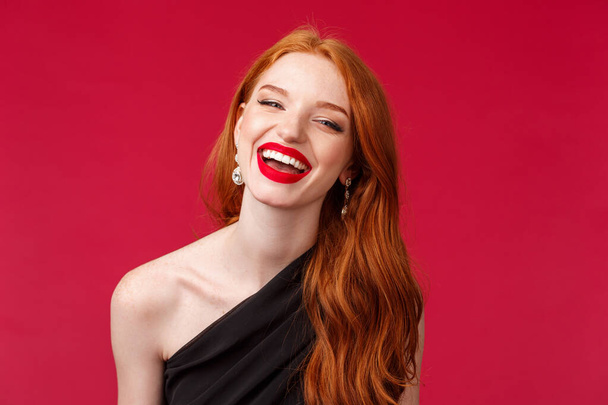 Romantiek, elegantie, schoonheid en vrouwelijk concept. Close-up portret van vrolijke, vrolijke roodharige vrouw in luxe zwarte jurk, rode lippenstift, genieten van feest of date, lachen stralende glimlach - Foto, afbeelding
