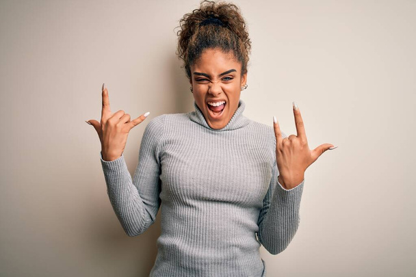 Beautiful african american girl wearing turtleneck sweater standing over white background shouting with crazy expression doing rock symbol with hands up. Music star. Heavy concept. - Foto, afbeelding