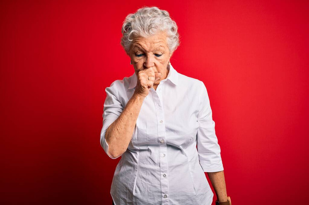 Senior mooie vrouw dragen elegante shirt staan over geïsoleerde rode achtergrond gevoel onwel en hoesten als symptoom voor koude of bronchitis. Gezondheidszorgconcept. - Foto, afbeelding