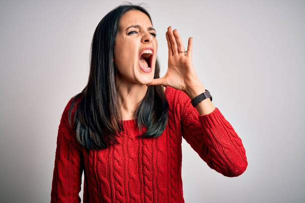 Young brunette woman with blue eyes wearing casual sweater over isolated white background shouting and screaming loud to side with hand on mouth. Communication concept. - Photo, Image