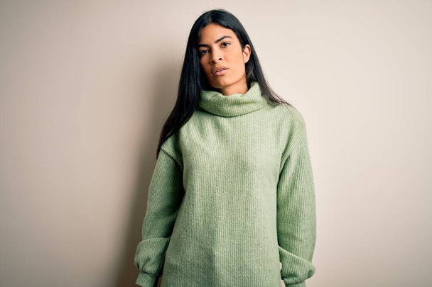 Young beautiful hispanic woman wearing green winter sweater over isolated background Relaxed with serious expression on face. Simple and natural looking at the camera. - Foto, imagen