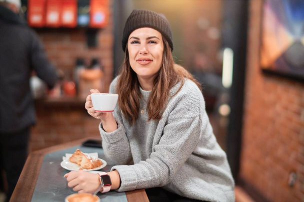 Young beautiful woman smiling happy and confident. Sitting at coffee shop holding a cup of coffee - Foto, imagen