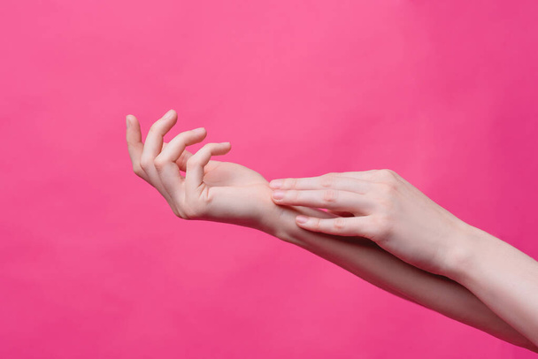 Mooie, jonge vrouwelijke handen op een roze achtergrond. Hygiëne, frisheid en huidverzorging concept, handen van een massage therapeut of cosmetoloog, industrie van schoonheidssalons en kuuroorden - Foto, afbeelding