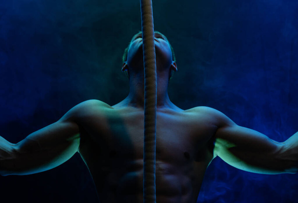 Muscular male circus artist with Cord Lisse on black an smoked background - Fotó, kép