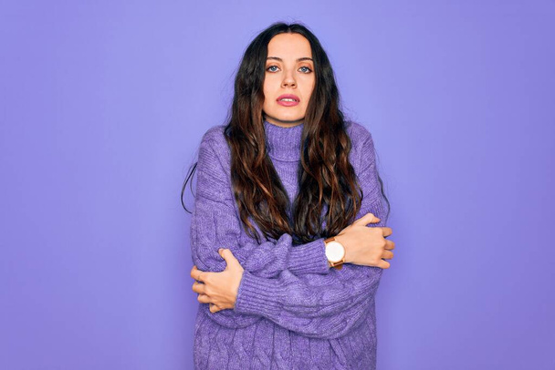 Young beautiful woman wearing casual turtleneck sweater standing over purple background shaking and freezing for winter cold with sad and shock expression on face - Photo, Image