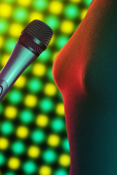 Primer plano de la cantante de pie junto al micrófono vocal iluminado por brillantes luces de discoteca en el fondo. Música, canto, disco, karaoke y reproducción de sonido
. - Foto, Imagen