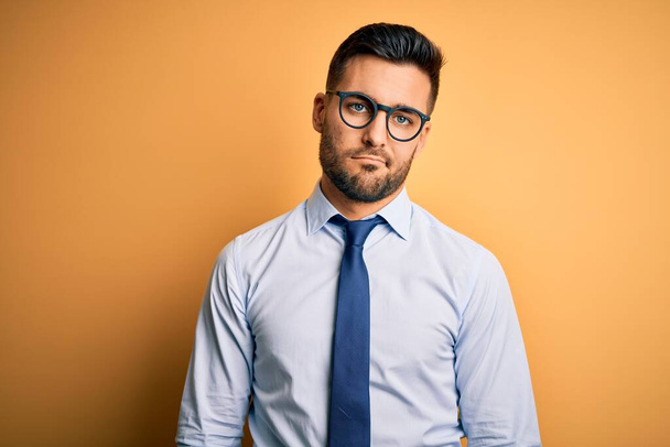 Young handsome businessman wearing tie and glasses standing over yellow background looking sleepy and tired, exhausted for fatigue and hangover, lazy eyes in the morning. - Photo, Image