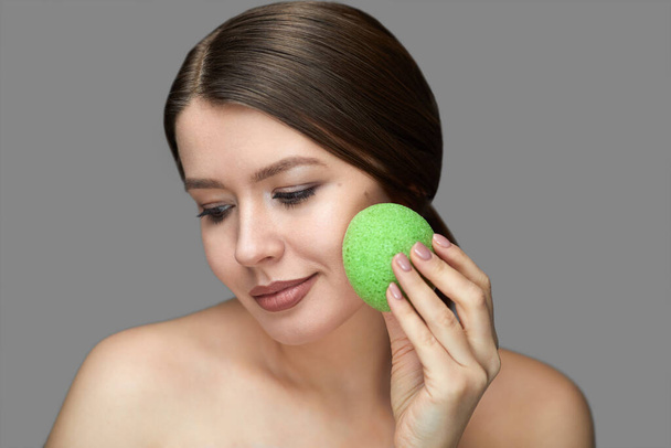 menina fazer um tratamento facial com uma esponja konjac verde em um fundo cinza com o lugar para tex
 - Foto, Imagem