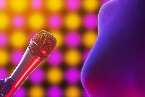Primer plano de la mujer de pie junto al micrófono vocal iluminado por luces de discoteca en el fondo. Música, canto, disco, karaoke y reproducción de sonido
. - Foto, Imagen
