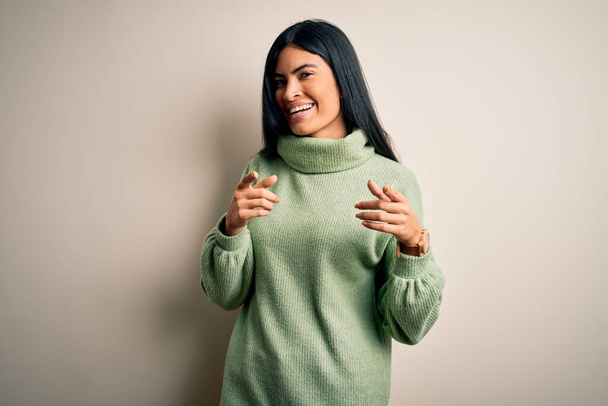 Young beautiful hispanic woman wearing green winter sweater over isolated background pointing fingers to camera with happy and funny face. Good energy and vibes. - Photo, Image
