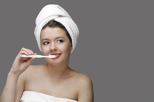 girl with a white toothbrush in a towel on her head on a grey background with the place for tex - Foto, Bild