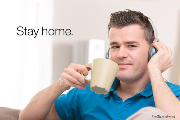 mężczyzna pijący gorący napój z kubka i słuchający muzyki ze słuchawkami w domu, aby uniknąć COVID19 koronawirusa - Zdjęcie, obraz