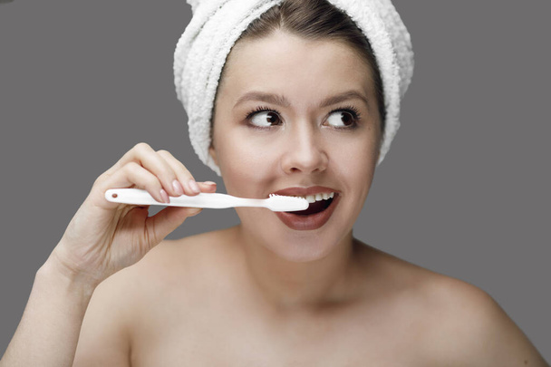 dziewczyna z białą szczoteczką do zębów w ręczniku na głowie na szarym tle z miejscem dla tex - Zdjęcie, obraz