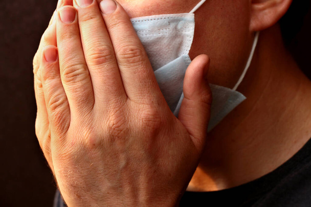 man niest draagt een medisch masker - Foto, afbeelding