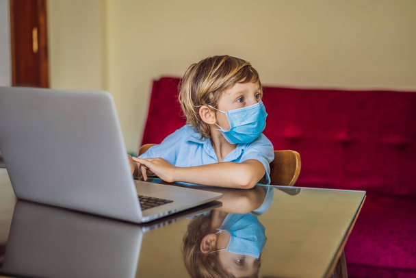 Boy studying online at home using laptop in medical masks to protect against coronovirus. Studying during quarantine. Global pandemic covid19 virus - Photo, image