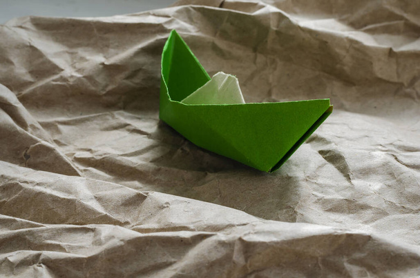 Un viejo barco de papel sobre olas de papel. Origami de papel verde atascado y desgarrado. Concepto de logro de metas. Disparo a nivel de ojos. Vista lateral. Enfoque selectivo
. - Foto, imagen