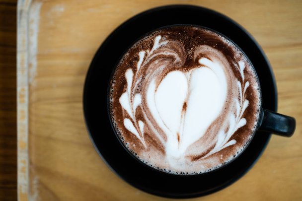 Sztuka latte w kształcie serca z filiżanką ciemnej czekolady na drewnianym stole. Napój spieniony na przerwę na gorący napój po pracy lub spotkaniu weekendowym - Zdjęcie, obraz