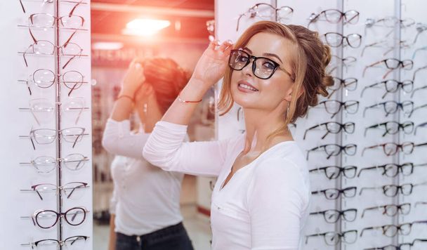Beautiful young woman choosing new pair of spectacles in opticians store. Eyesight correction. Optics. Ophthalmology. - Valokuva, kuva