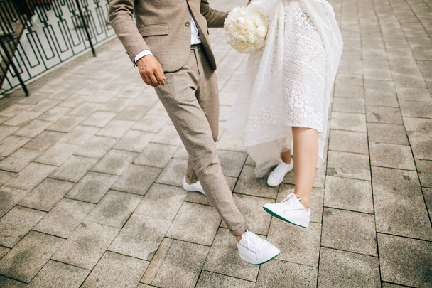 Bride and groom on the street show their shoes. Not classic wedding shoes - Photo, Image