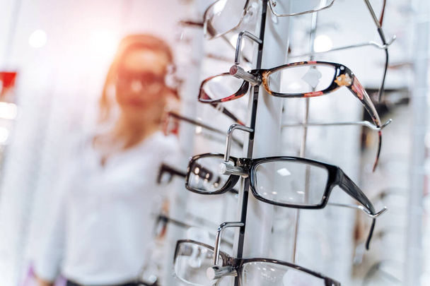 Stand with glasses in the store of optics. Woman chooses glasses. - Foto, Imagen