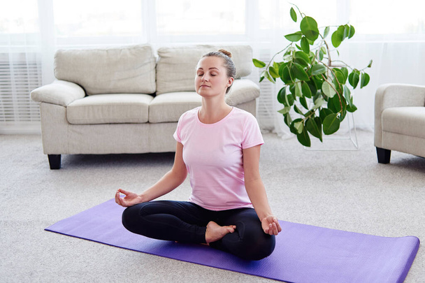 Girl sitting in lotus position and meditating at home interior, copy space. Padmasana. Woman practicing home yoga. Close up hands in meditating gesture. Freedom concept - Photo, Image