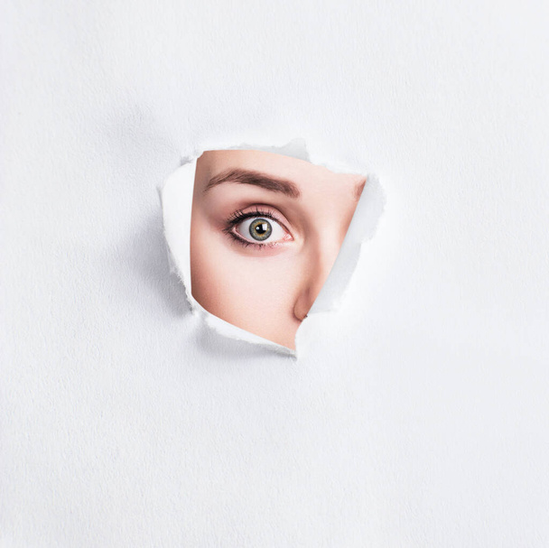 Surprised woman peeps into the slit of white paper. - Fotografie, Obrázek