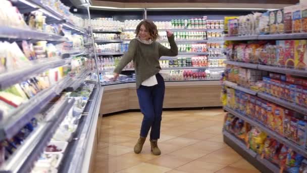 Повний запис про молоду жінку, що танцює через проходи продуктового магазину. Задоволена жінка розважається, танцює супермаркет. Повільний рух - Кадри, відео