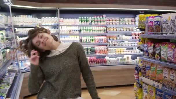 Portrait of young woman with shirt curly hair dancing standing at grocery store aisle. Excited woman having fun, dancing supermarket, smiling. Slow motion - Filmati, video