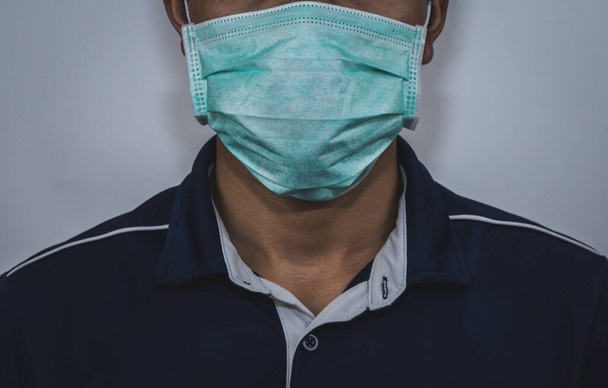 Een jonge Aziatische man is ziek als gevolg van virussen infectie en draagt een chirurgisch masker om te voorkomen dat de kiemen verspreiden in de lucht om anderen te infecteren. Een Aziatische man infecteert met virussen en draagt een masker. - Foto, afbeelding