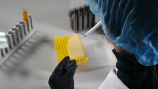 Back view of female scientist dropping chemical liquid in test tubes. Close up of scientist hands working with chemical reagents in laboratory glassware. 4k - Felvétel, videó