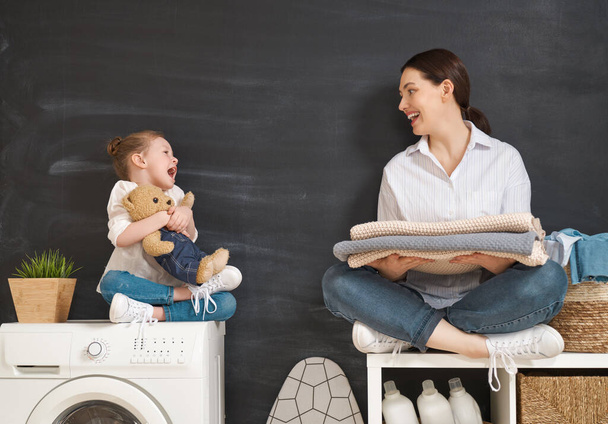 Beautiful young woman and child girl little helper are having fun and smiling while doing laundry at home.  - Φωτογραφία, εικόνα