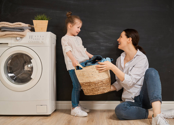 Beautiful young woman and child girl little helper are having fun and smiling while doing laundry at home.                                 - Foto, Imagem