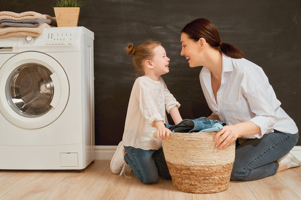 Beautiful young woman and child girl little helper are having fun and smiling while doing laundry at home.                                 - Foto, imagen