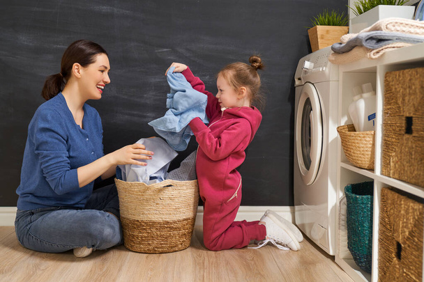Beautiful young woman and child girl little helper are having fun and smiling while doing laundry at home.                                 - Fotó, kép